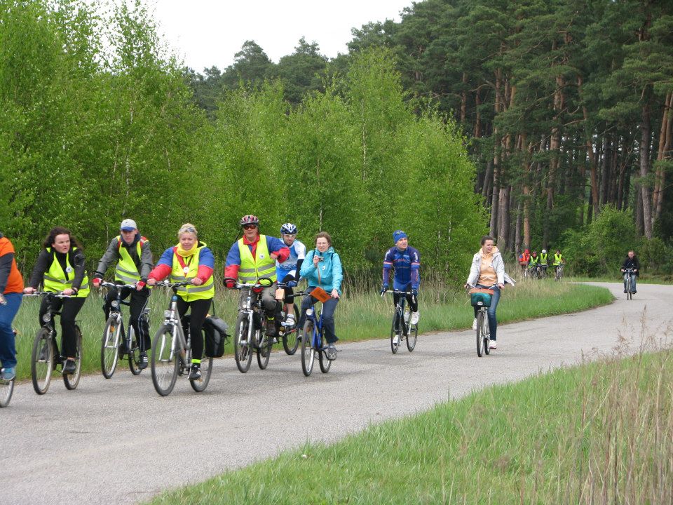 Kilkanaście osób ubranych w kurtki jedzie na rowerach. 